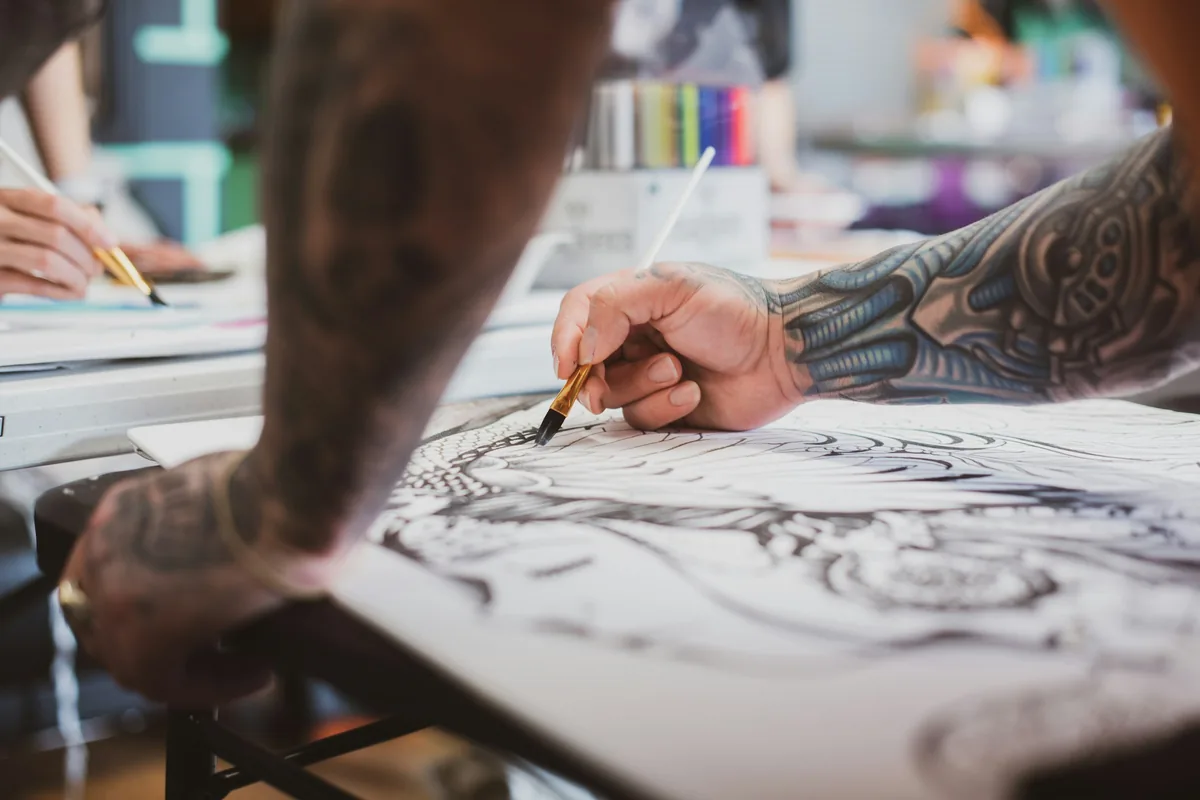 Tattooed artist drawing one of a client's tattoo ideas as a detailed design on paper
