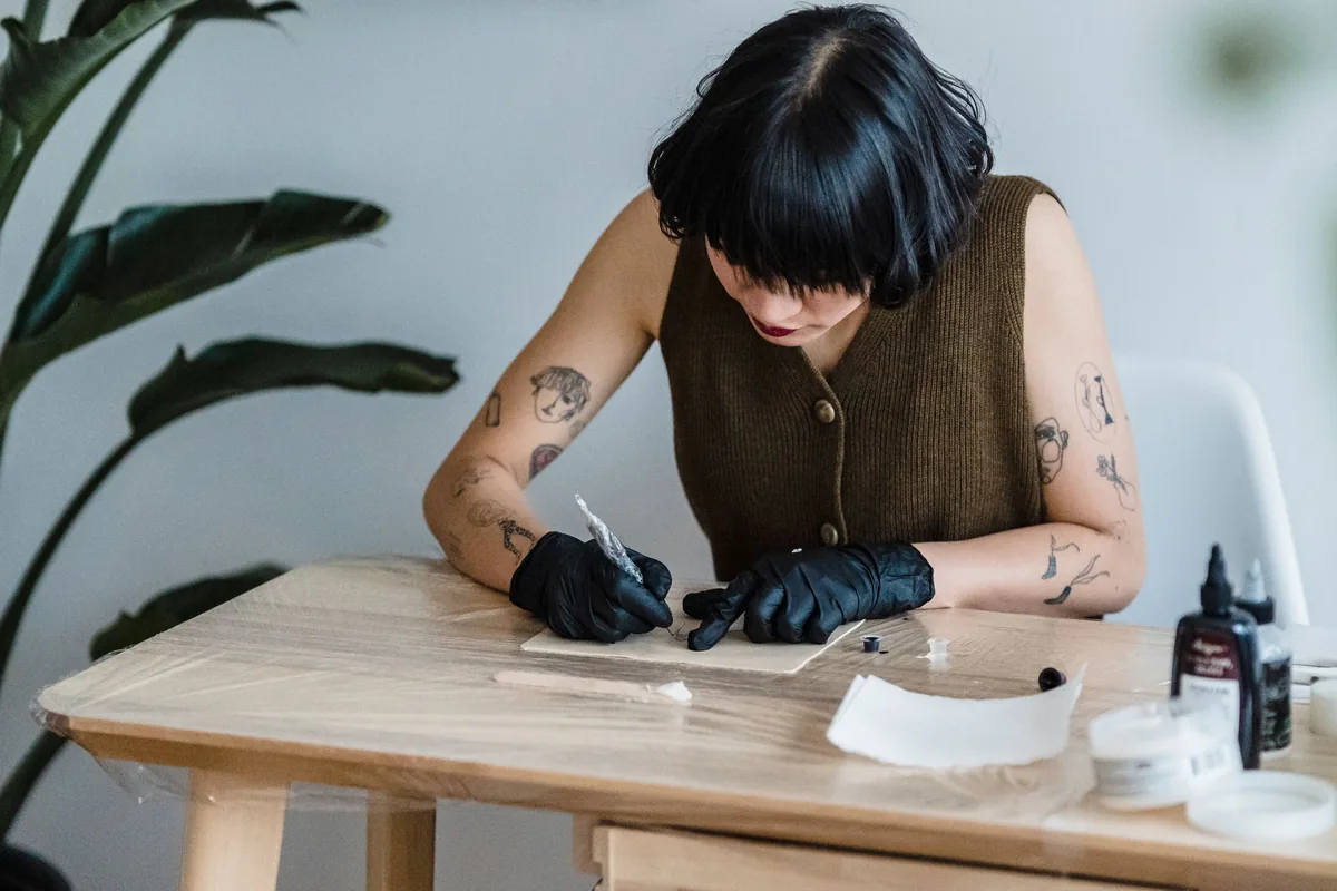 Artist sketching a tattoo design at a wooden table, ready to contact Tattoo Malaysia with a correction