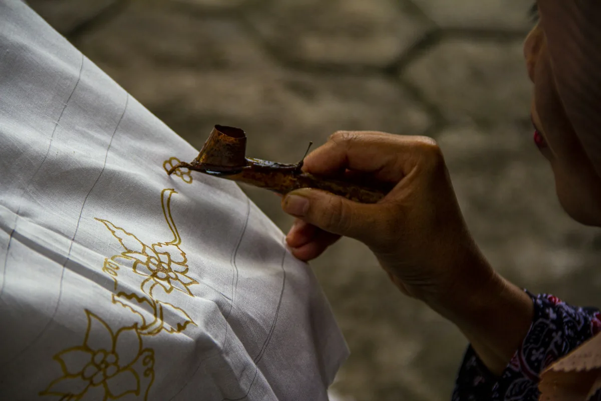 Artisan drawing a floral batik design with a canting tool, a craft that inspires many Malaysian tattoo designs