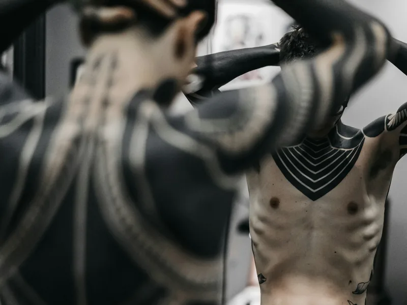 Bold blackwork tattoos across a man's back, arms and torso