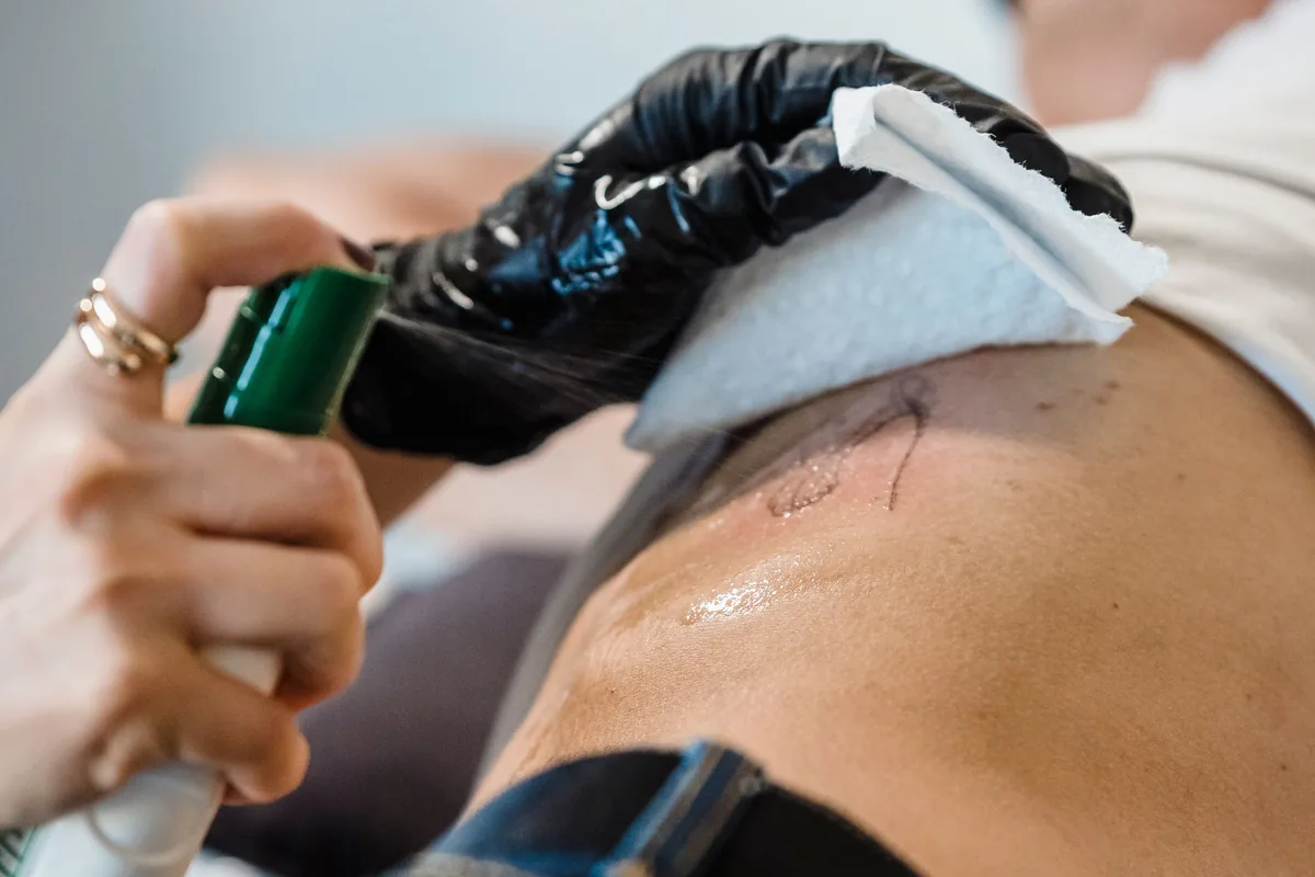 Tattooist wiping a fresh back tattoo clean with a paper towel before tattoo aftercare begins
