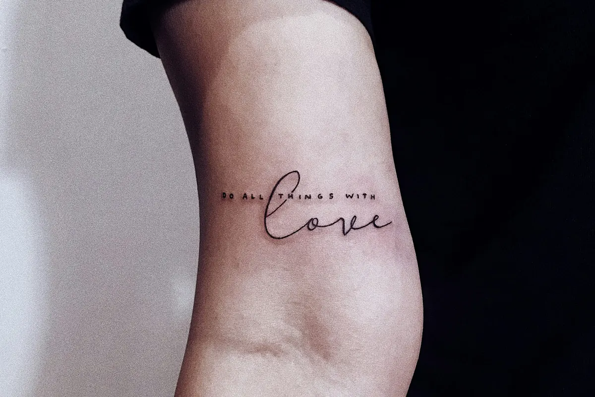 Delicate fine line script tattoo on the back of an arm, a popular choice among tattoo designs for women