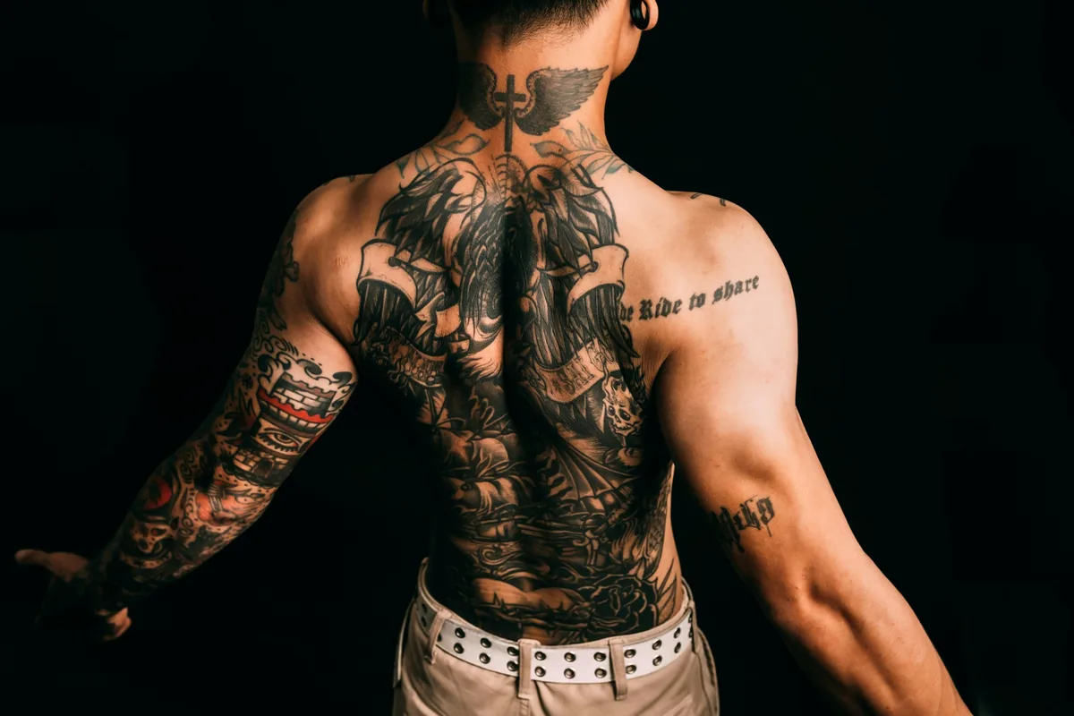 Man with a large back piece and full arm sleeves photographed against a dark background