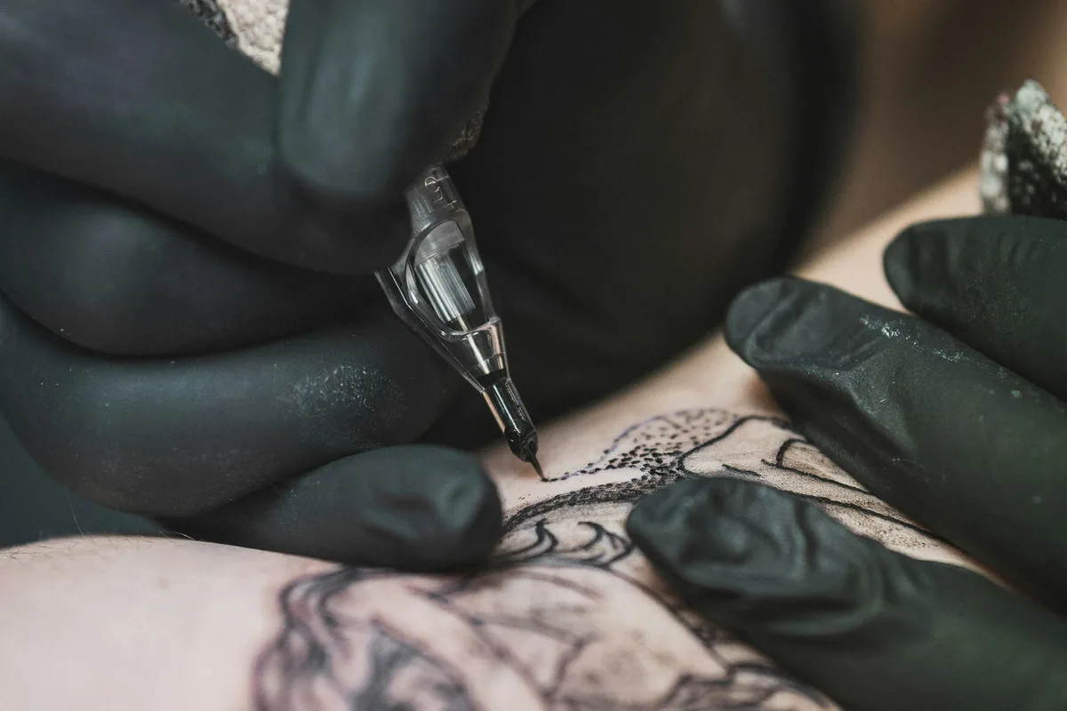 Gloved hands outlining a fine line tattoo design on skin