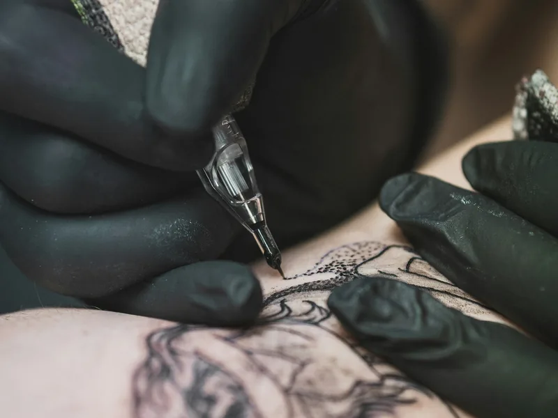 Gloved hands outlining a fine line tattoo design on skin