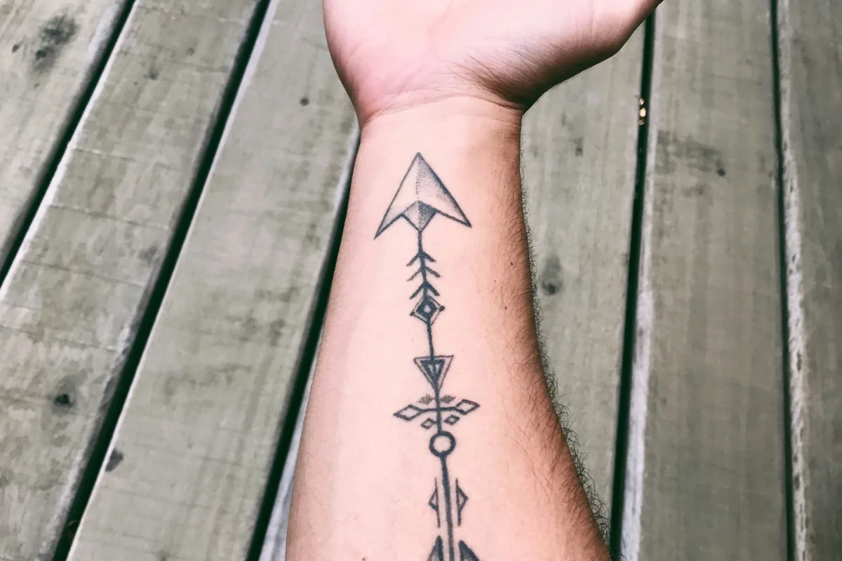 Minimalist tattoo of an arrow running down an inner forearm