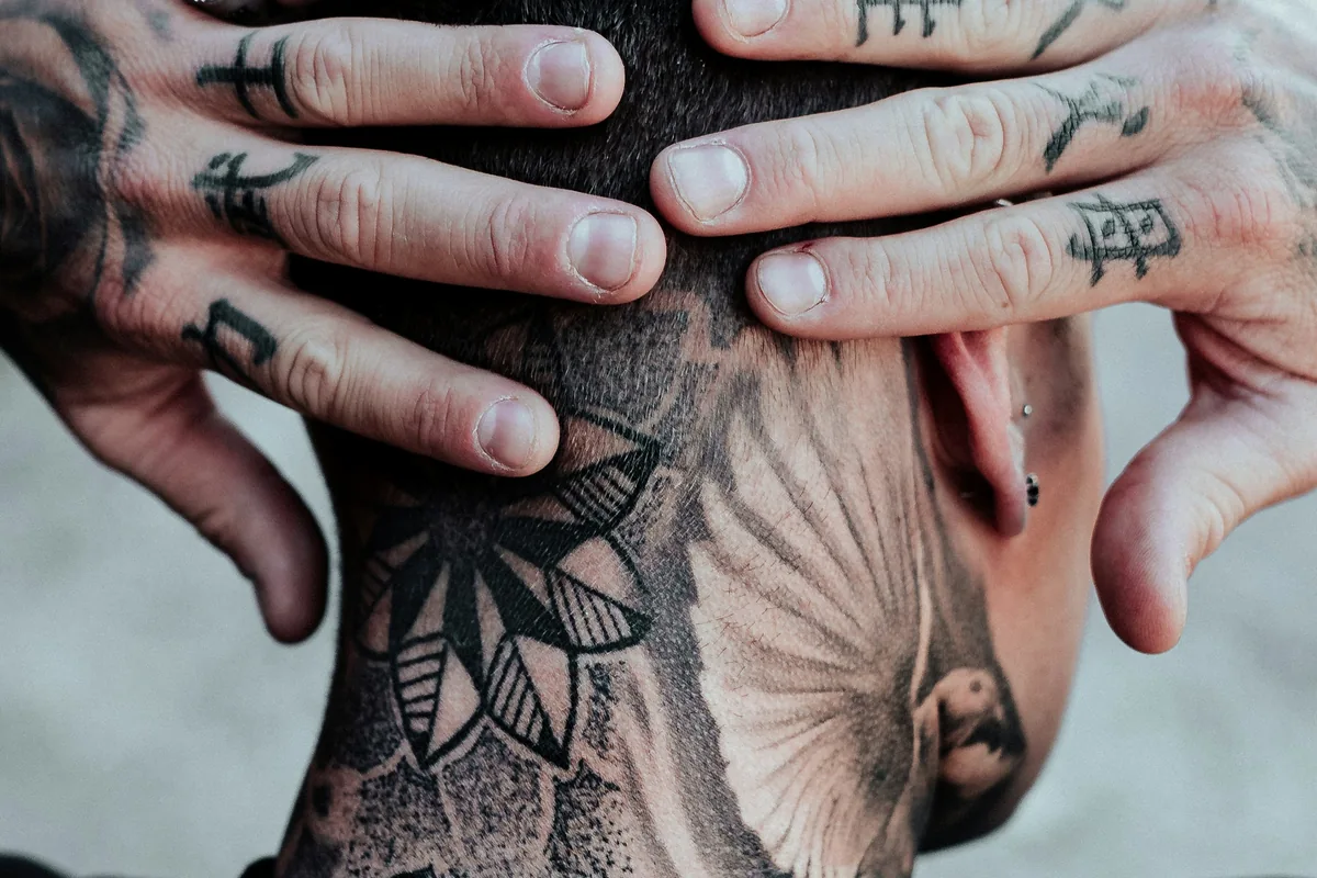 Person with tattoos on the neck, hands and fingers, showing how visible hand tattoo designs for men can be