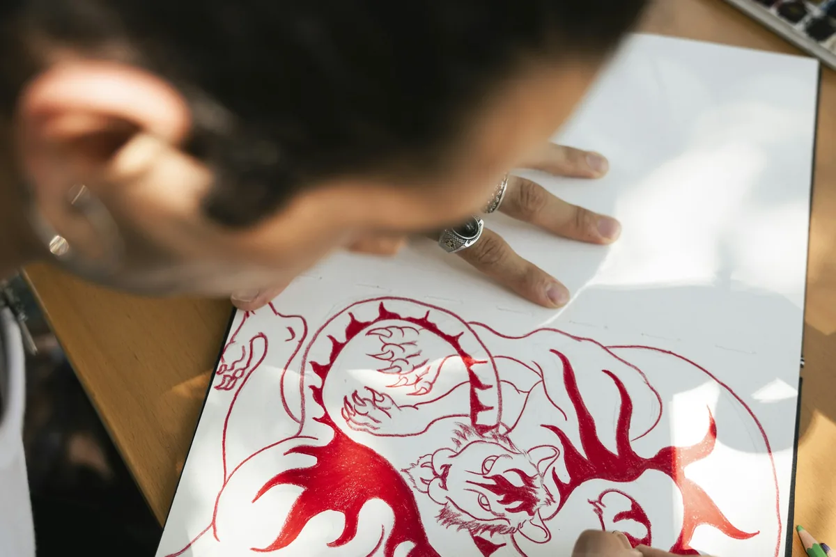 Artist sketching a red tiger design in a sketchbook, the kind of craft the Tattoo Malaysia blog explores