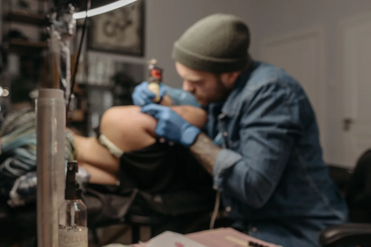 Tattoo artist working under a ring light with supplies on the desk, ready for a tattoo touch up session