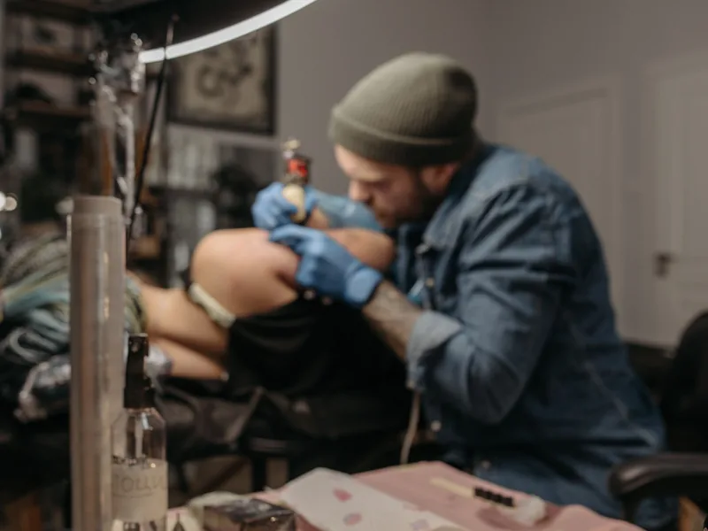 Tattoo artist working under a ring light with supplies on the desk, ready for a tattoo touch up session
