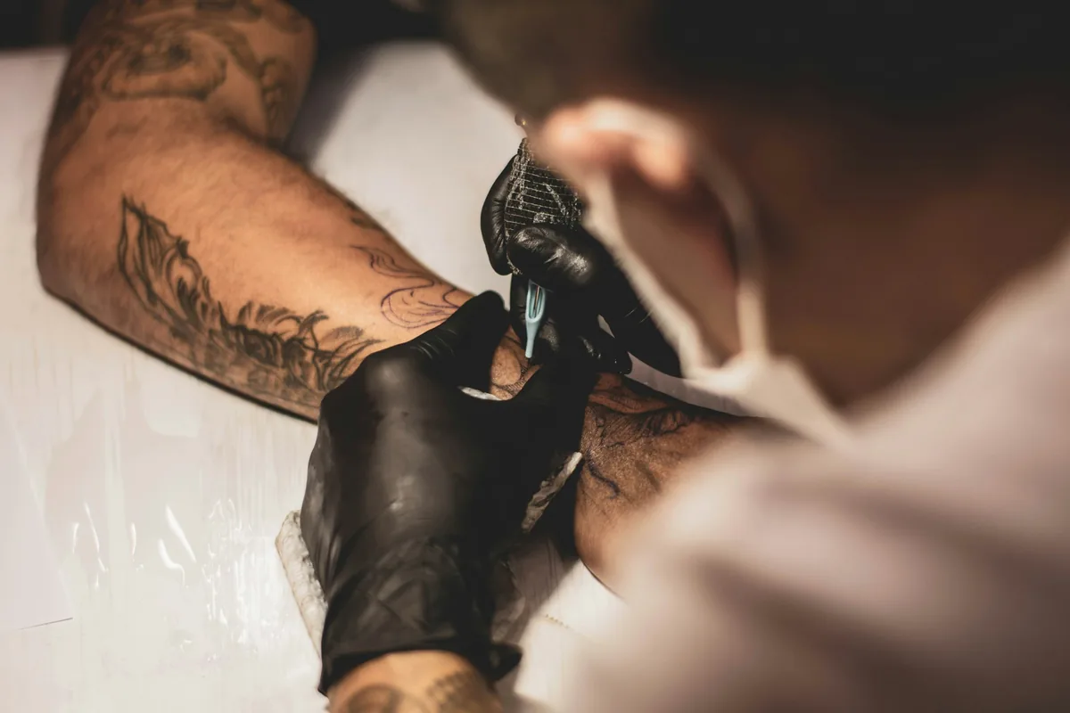 Tattooist in black gloves shading a client's forearm, the slow, detailed work that drives tattoo price in Malaysia