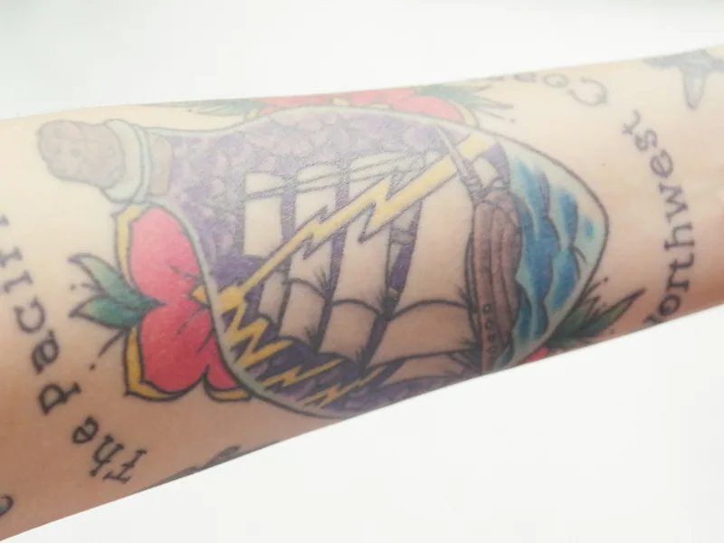 Colour traditional tattoo of a ship in a bottle with lettering on a forearm